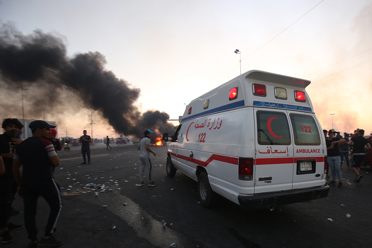 An ambulance in Baghdad protests with smoke and turmoil.