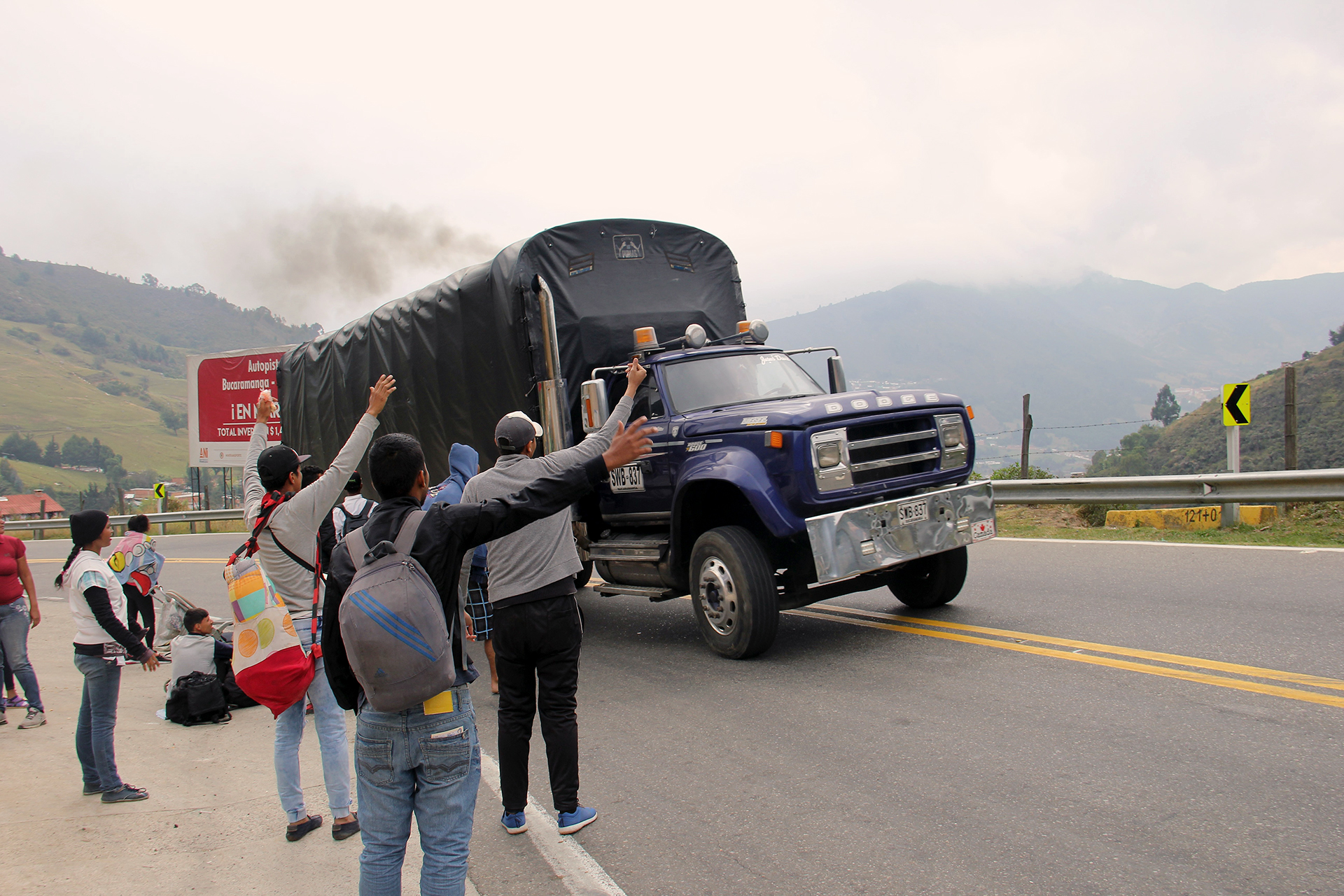 A group of people try to get rides on the side of a mountainous road