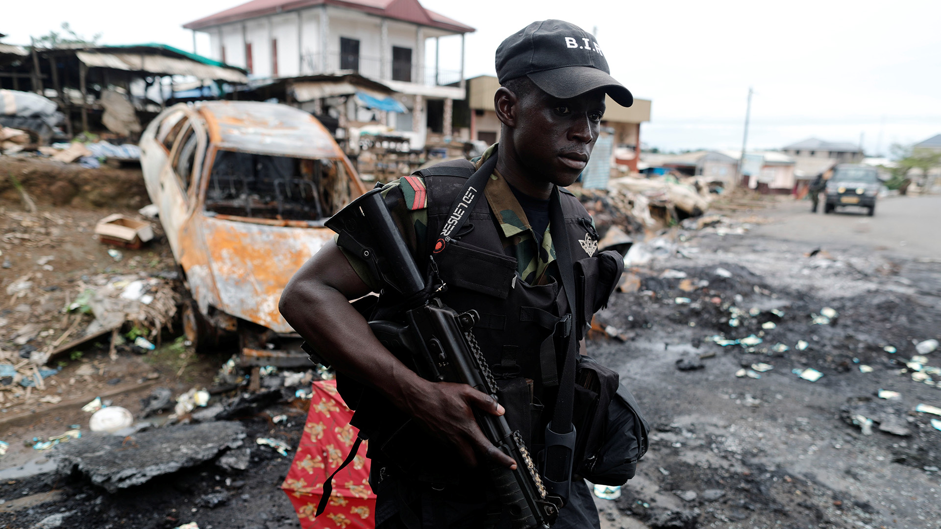 A Cameroonian government soldier walks past a burnt car