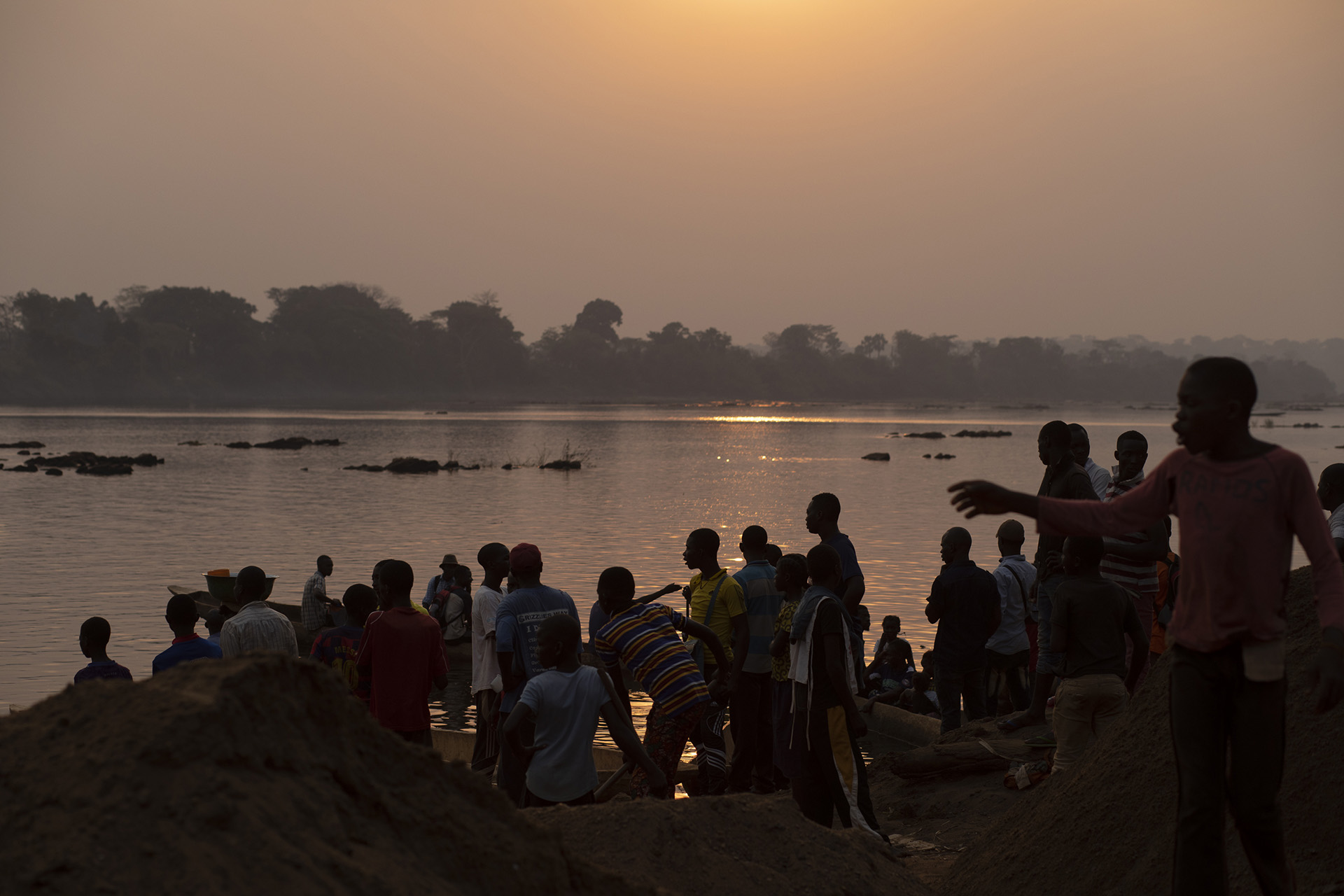 People stand on a riverbank in dim lighting.