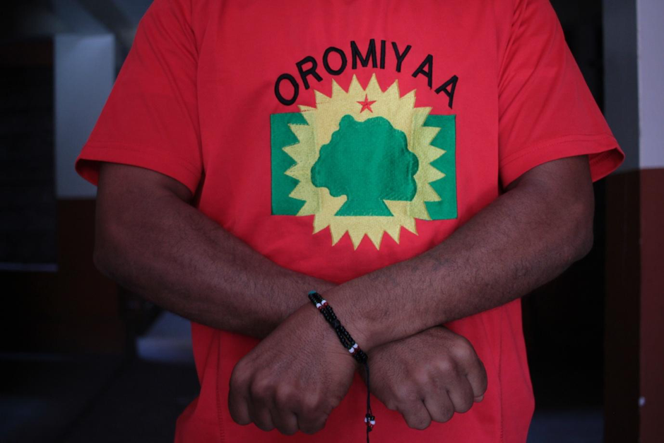A man with crossed arms wears a shirt that reads Oromiyaa