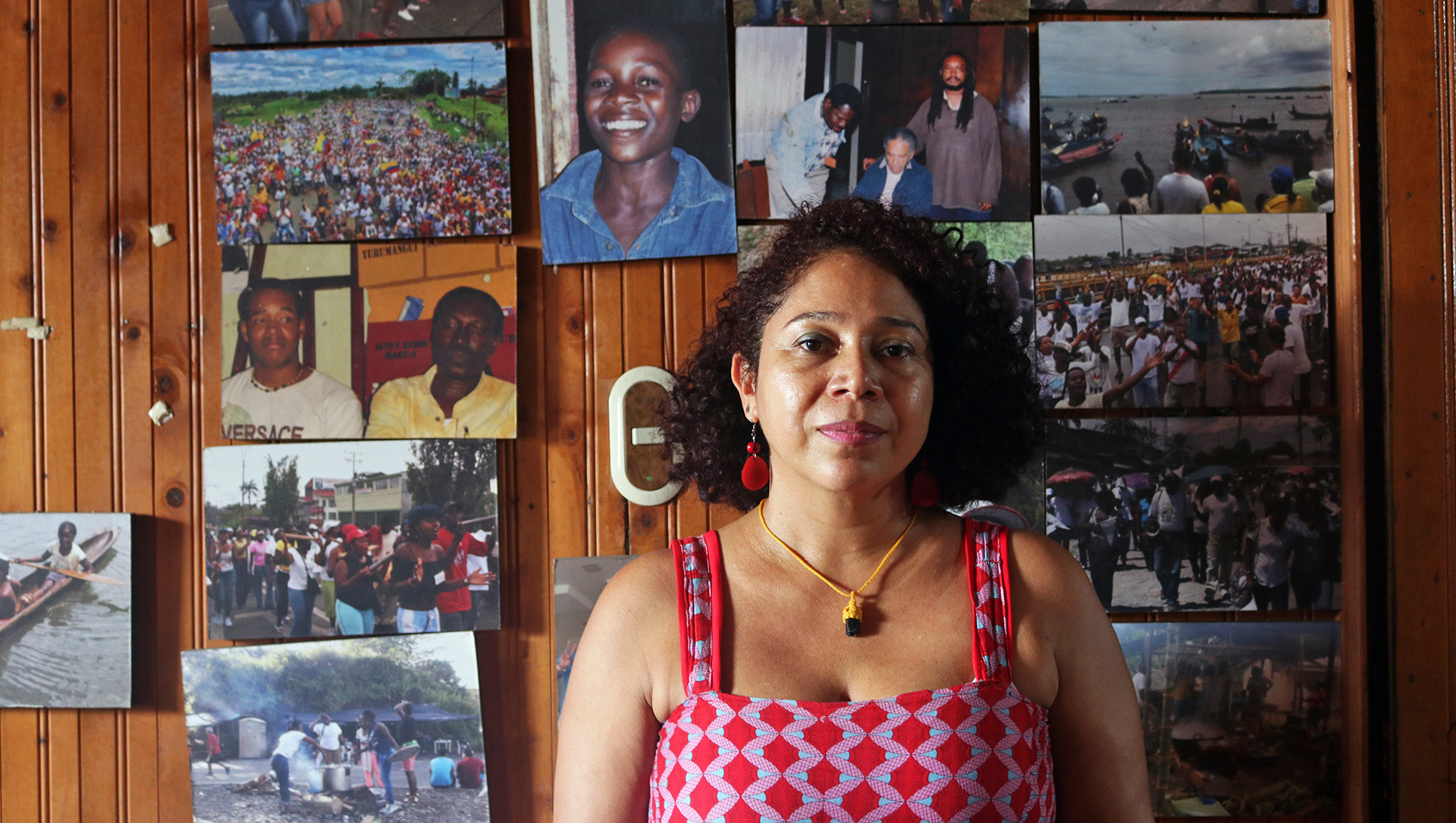 A portrait of Danelly Estupiñán standing against a wooden wall decorated with photographs
