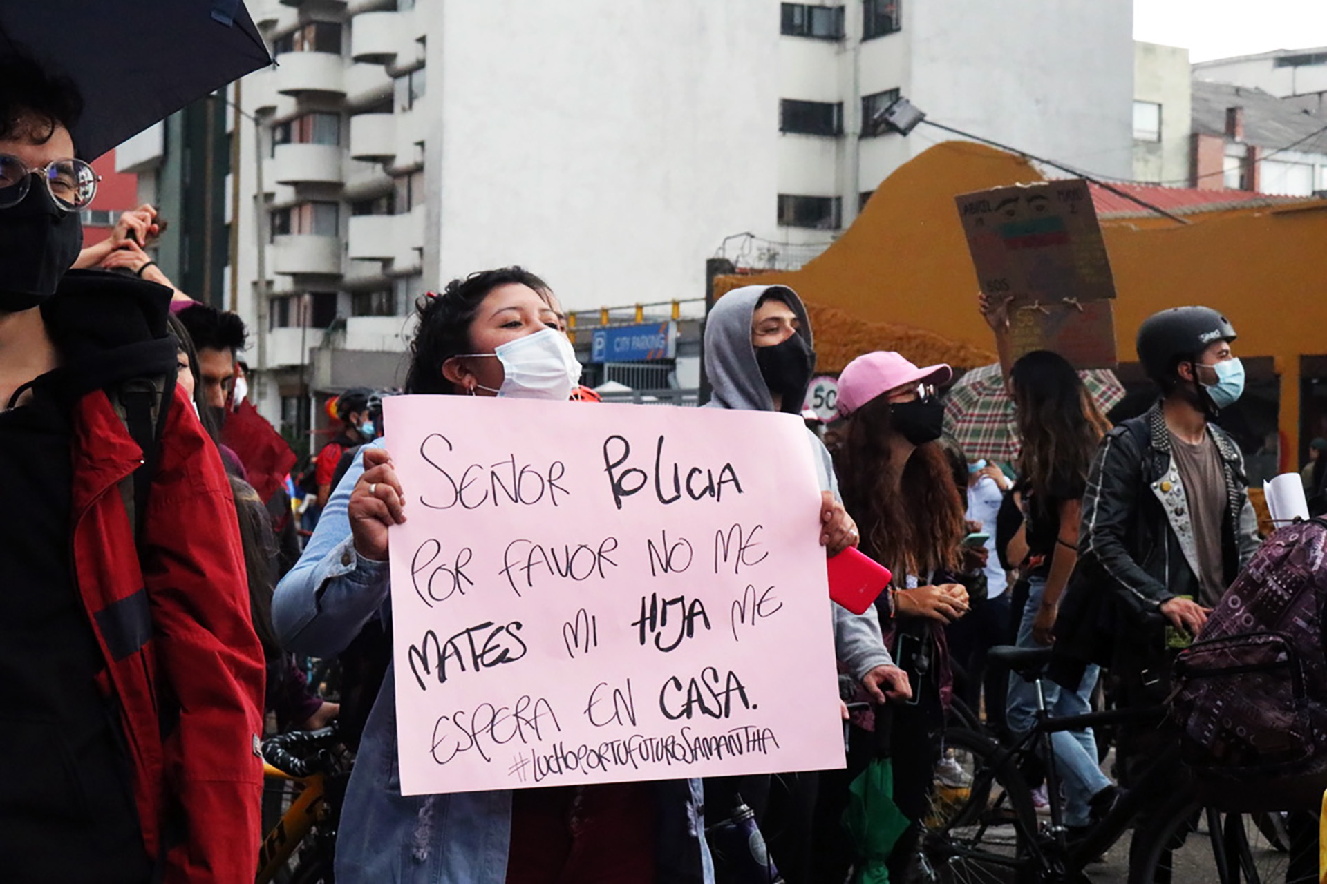 A woman wearing a mask holds a sign.