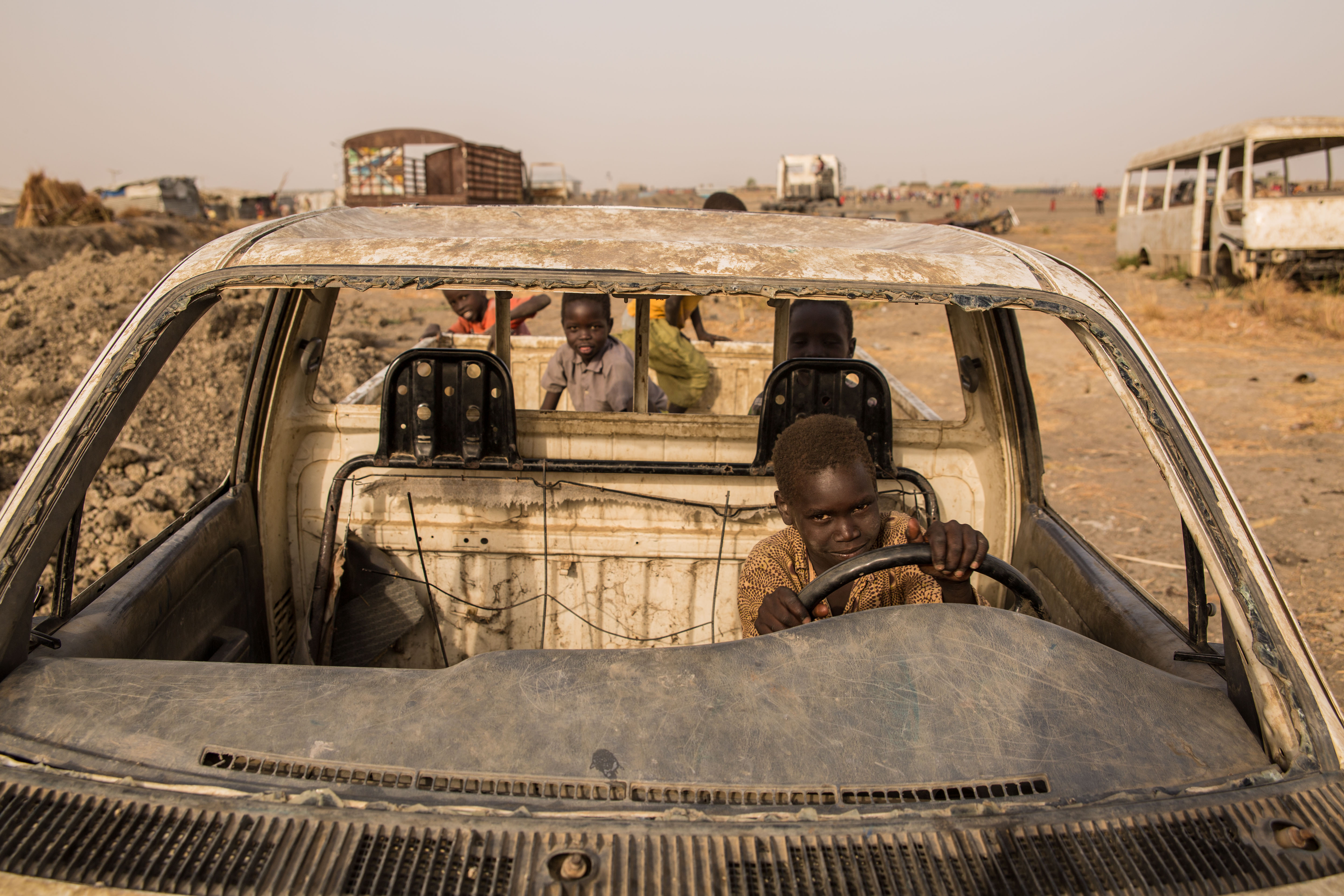 The front of a destroyed car with a child pretending to drive and children in the back of the car