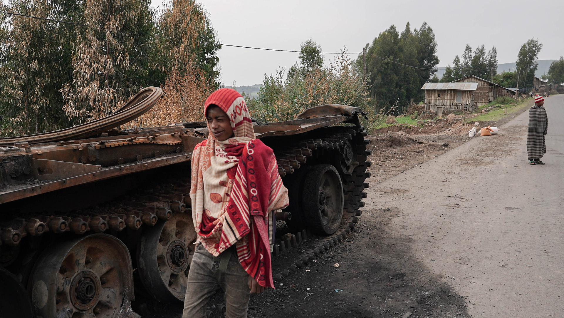 Residents walk past an abandoned tank on a main road in Amhara region, where hundreds of thousands of people have fled recent fighting.