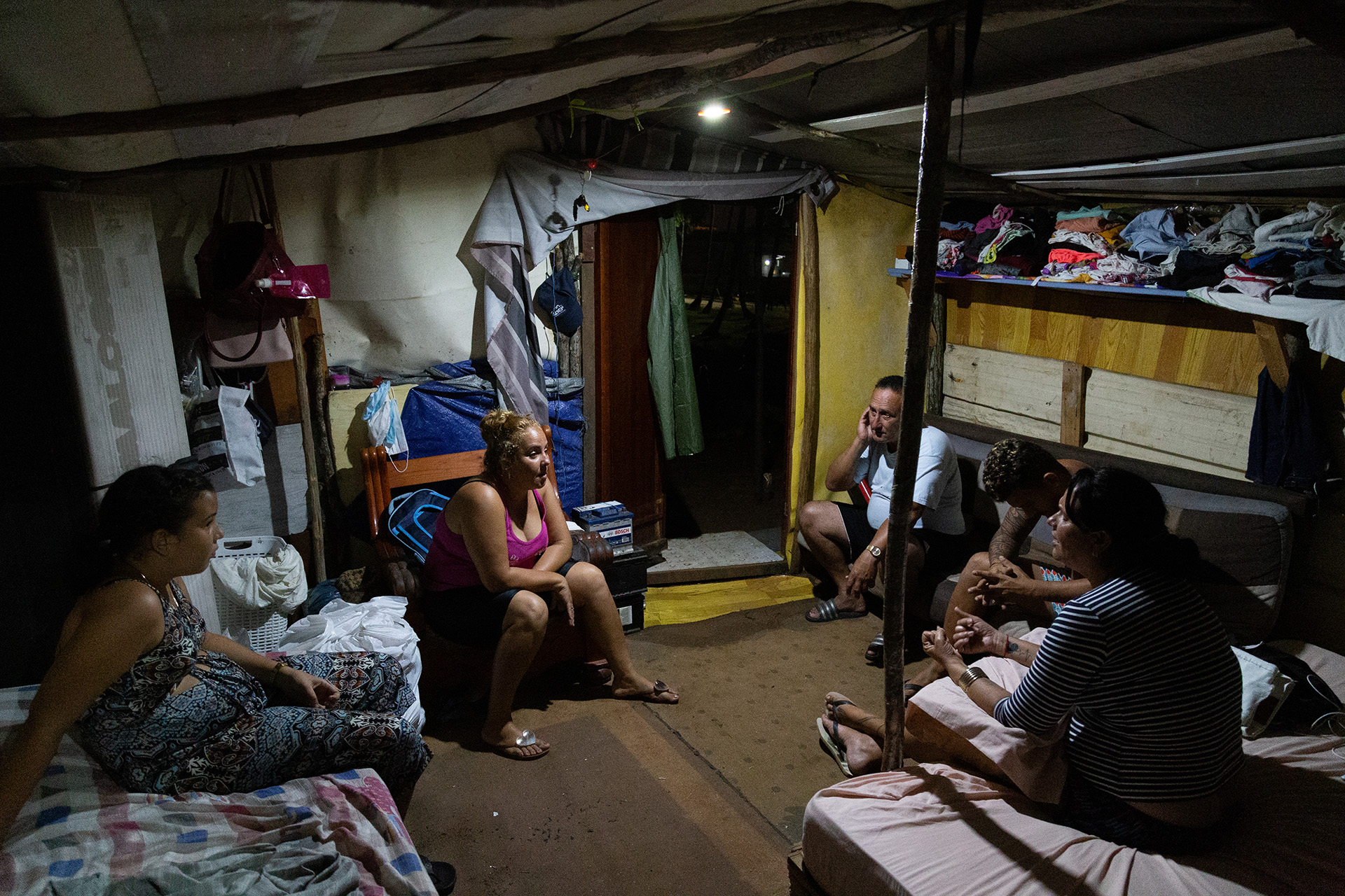 A family of Cuban migrants sits in a circle inside their tent talking in the evening.