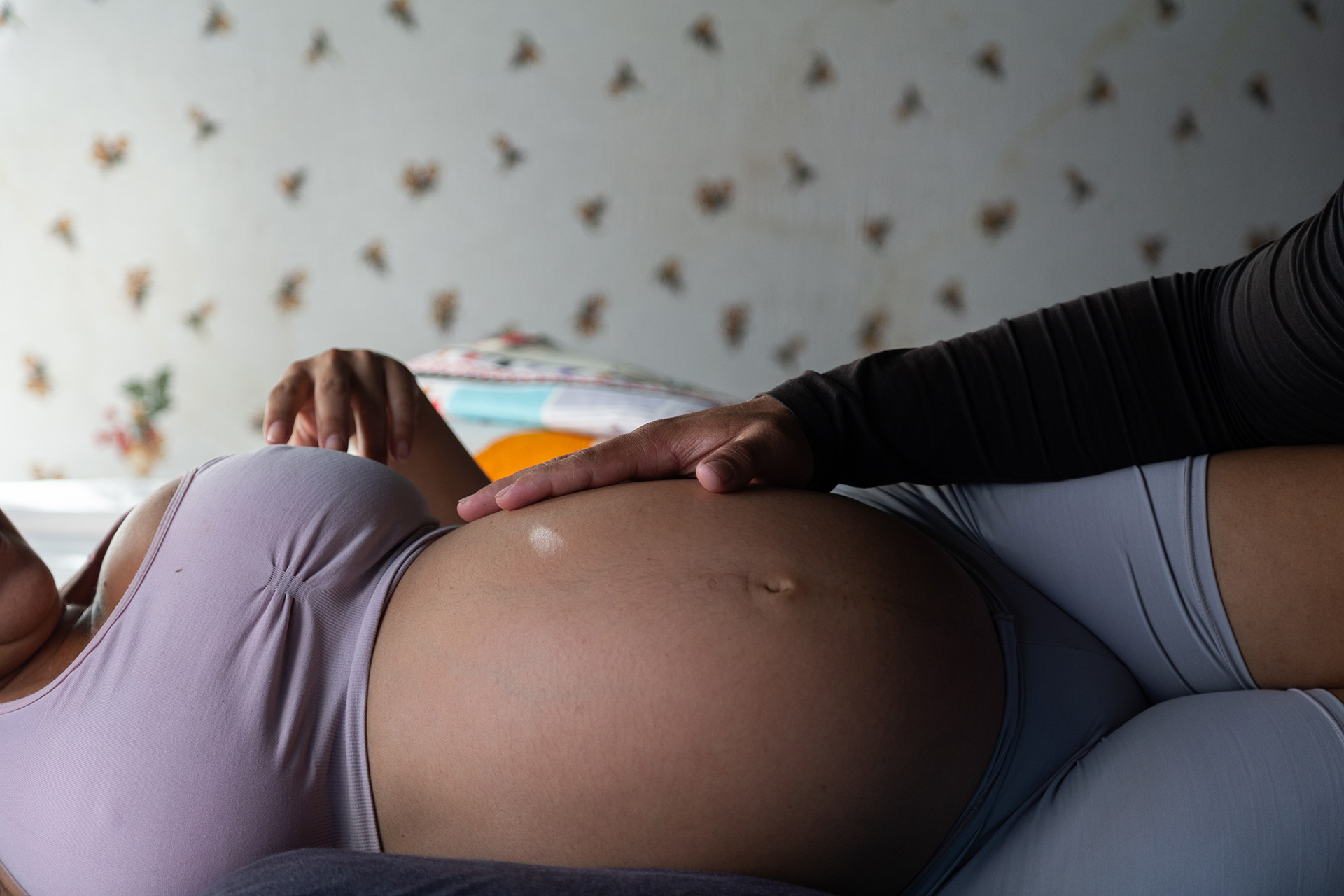 A close up image of a pregnant woman's stomach as she lies on a bed.