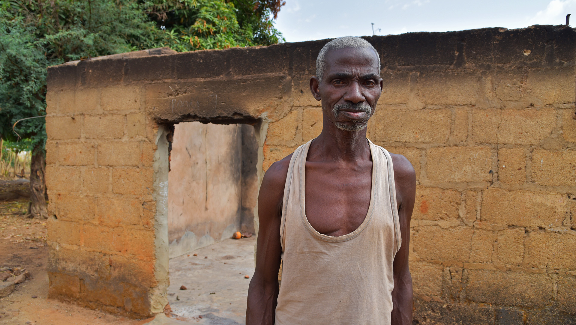 A man stands in front of a burnt out stone house
