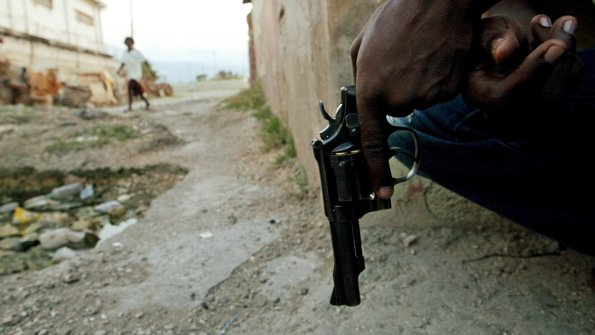 A pair of hands loosely holds a gun close to the ground.