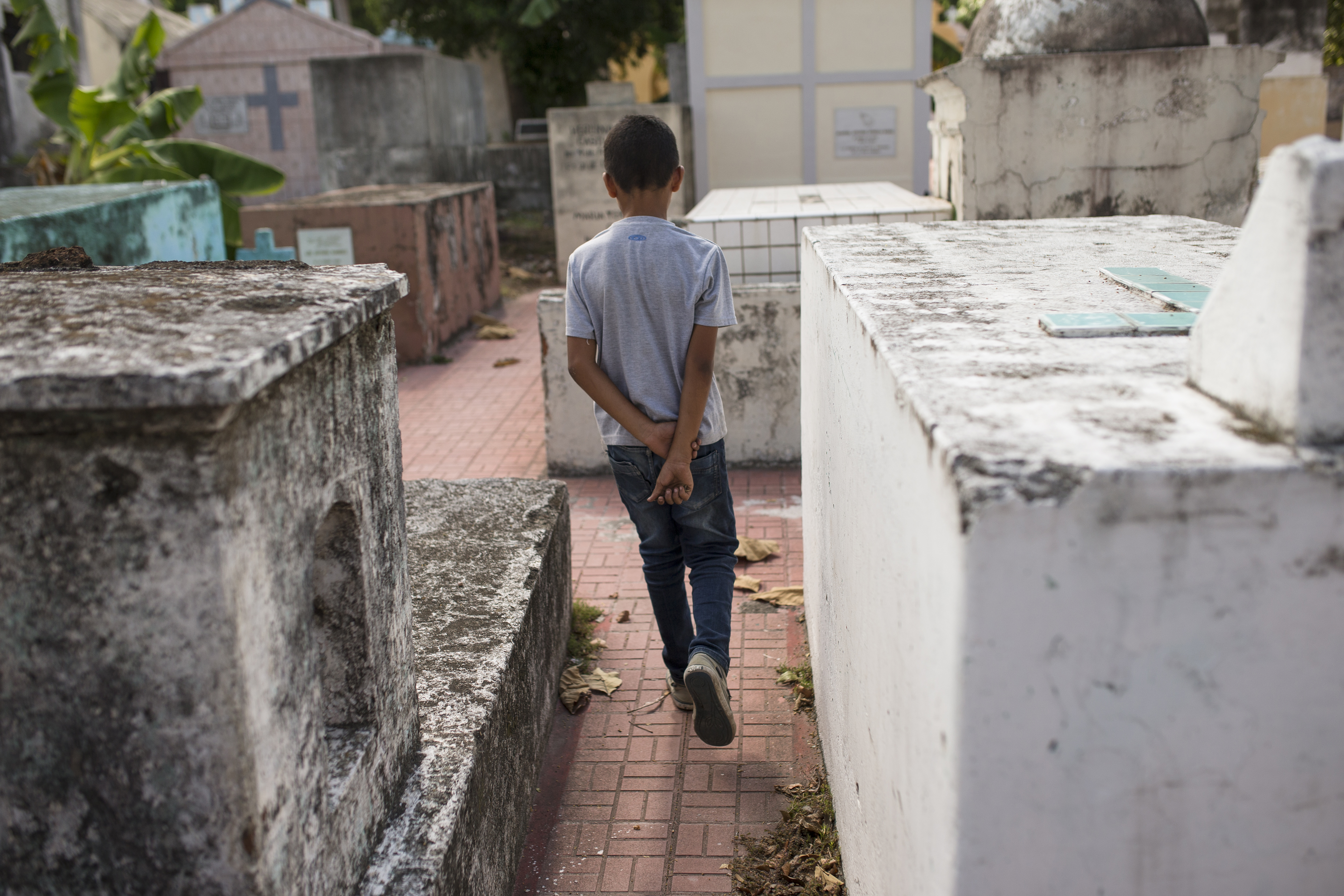 A boy walks through a cemetery in San Pedro Sula where he works at weekends offering grave cleaning services with his grandfather.
