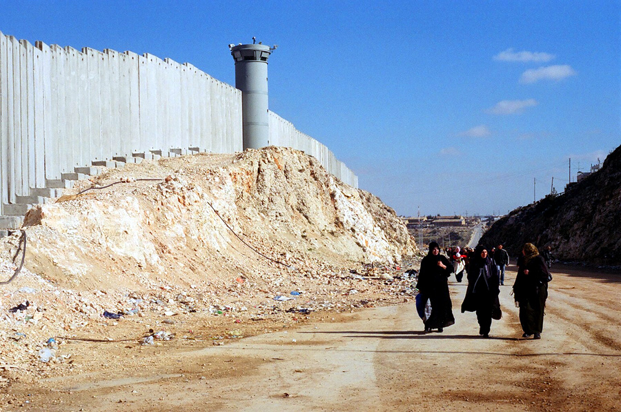 Palestinian women walk near Israel's barrier near Ramallah in the West Bank.