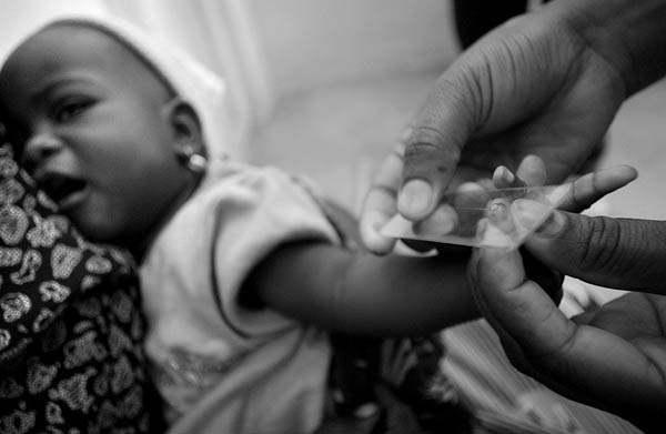 Nurse taking a blood sample from an infant for the malaria smear test. Paul Taggart, Malaria in Africa series, 2003