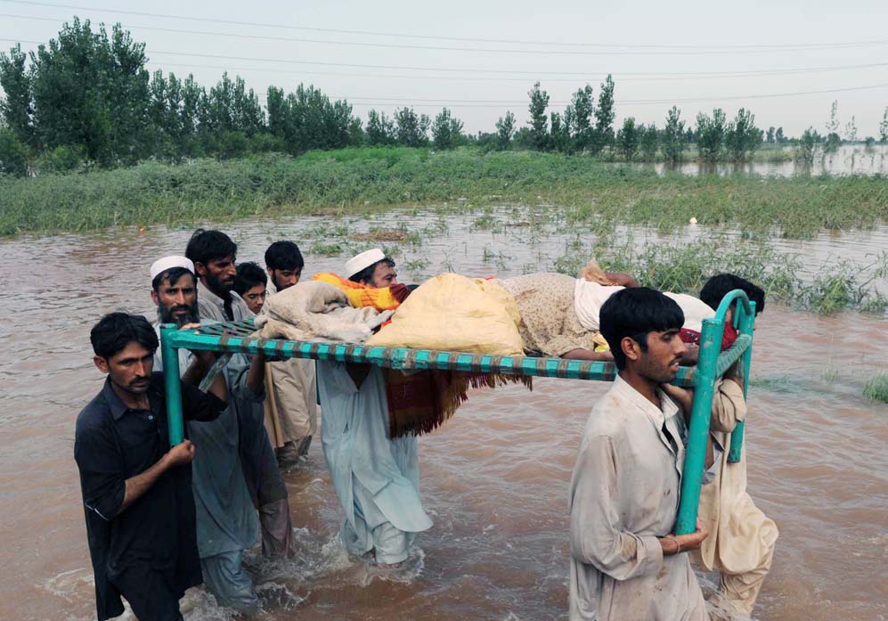 Flood victims in Khyber-Pakhtunkhwa carry an injured relative past destroyed fields