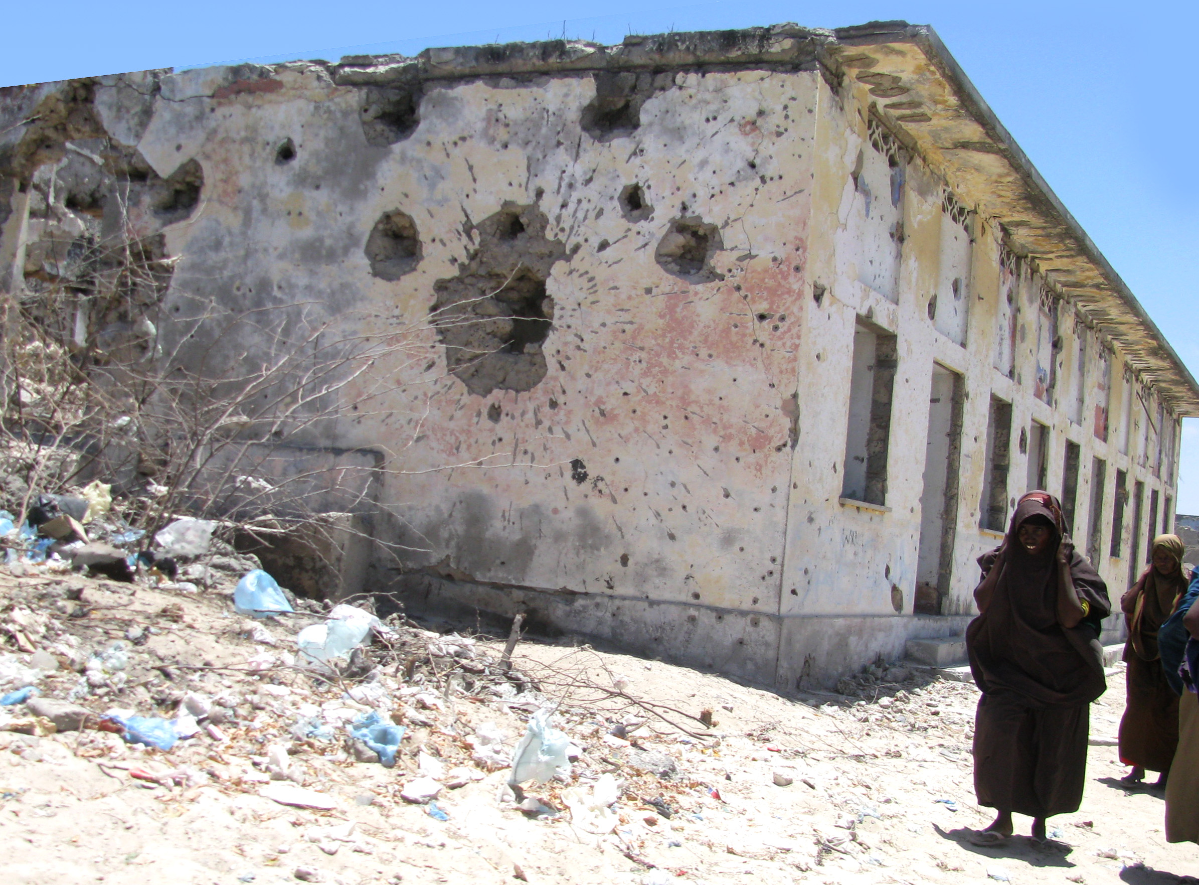 Women walk from Bakara market past a bullet-ridden building in Mogadishu