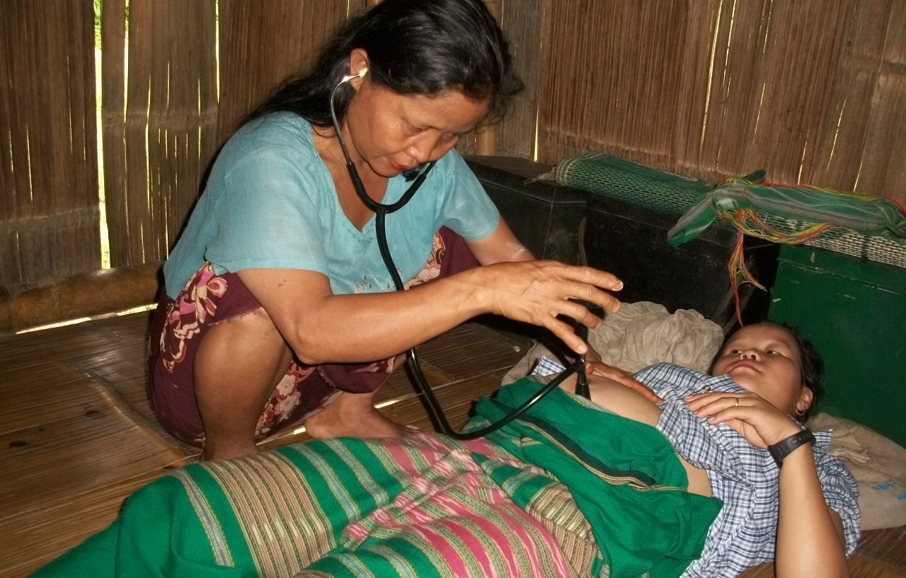 A traditional birth attendant examines a pregnant woman using a stethoscope in Karen state