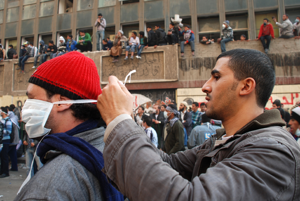 Two Egyptian men help each other fix papermasks used to protect against the tear gas-filled air in Cairo's Tahrir Square during protests against the ruling military council in November 2011
