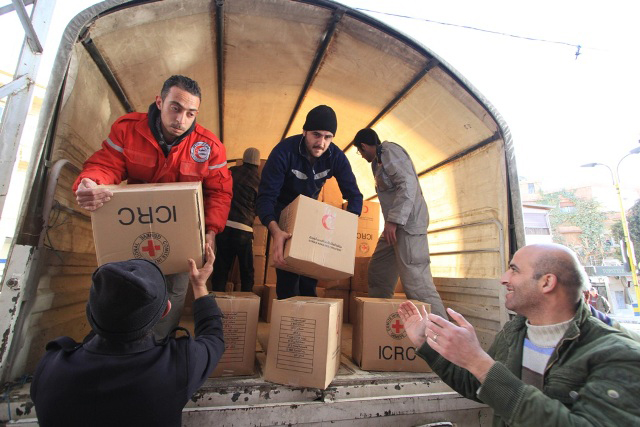 Local people help Syrian Arab Red Crescent volunteers unload food parcels from trucks in the main square of Bludan, Syria, at an impoverished warehouse donated by a local businessman
