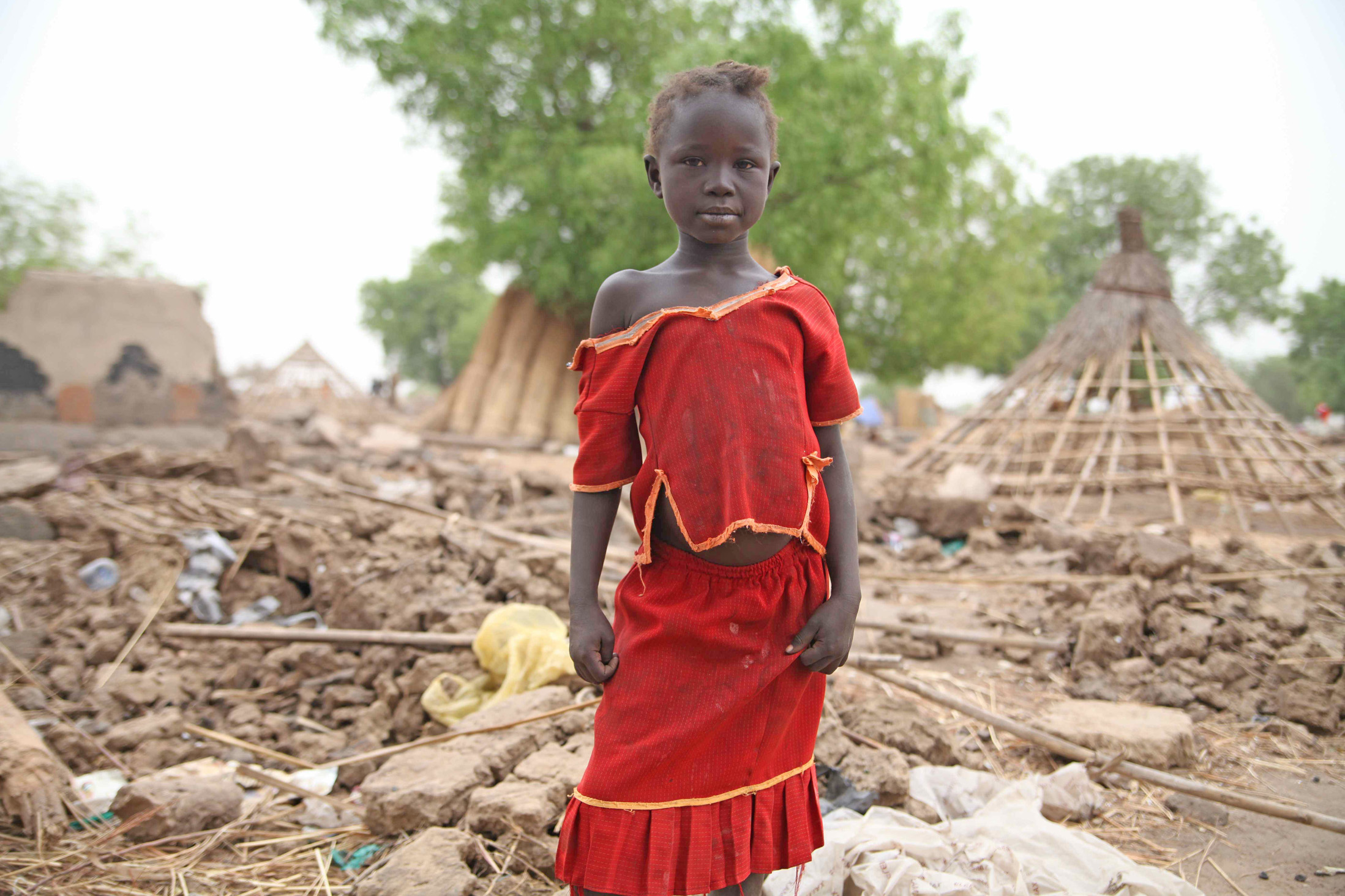 Small girl stands in the ruins of what was her home in South Sudan