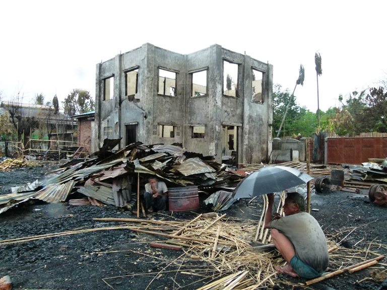 Two men sit under the the remnants of their homes in Sittwe, the capital of Myanmar's Rakhine State, following violence in June 2012.