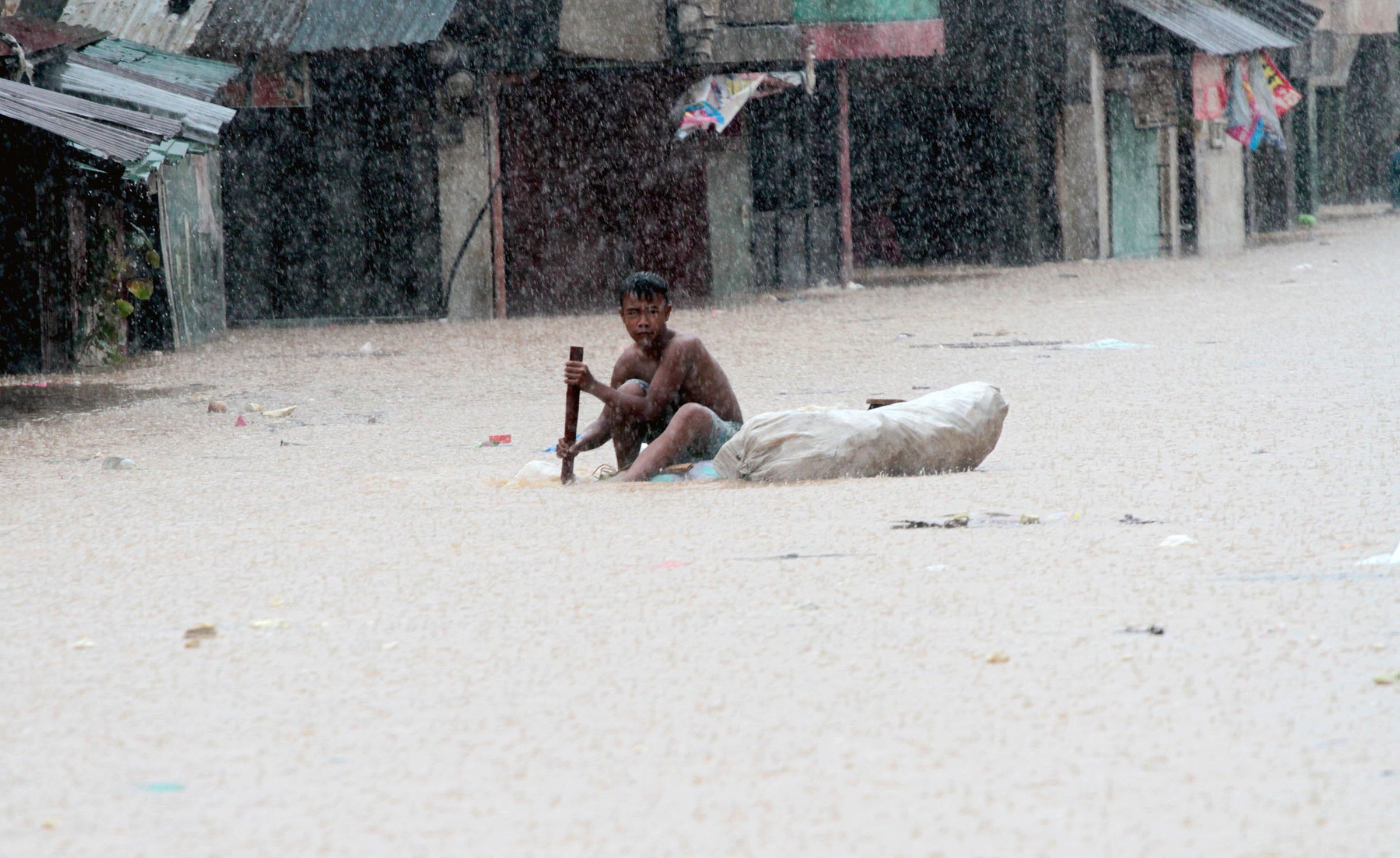 A boy on an improvised raft travels down a flooded road in a slum district of Tumana, near Marikina, in the Philippines (Aug 2012)
