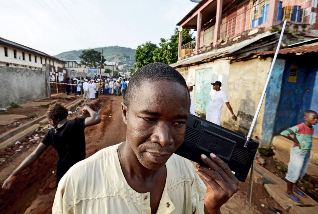 A man listens to the radio as people wait to vote in legislative and presidential elections 17 November 2012 in Fourah Bay, Freetown
