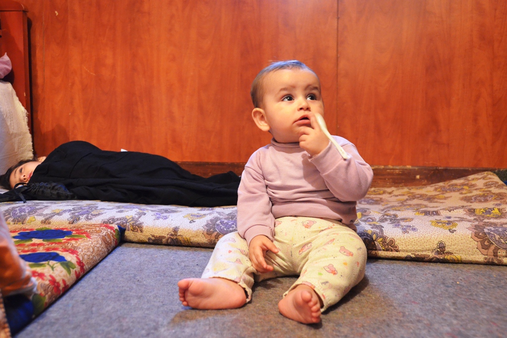 A 9-month old baby from Rural Damascus, Syria, sits on the floor of a room where his family has sought refuge in Tyre, South Lebanon, next to his cousin, sleeping on the floor