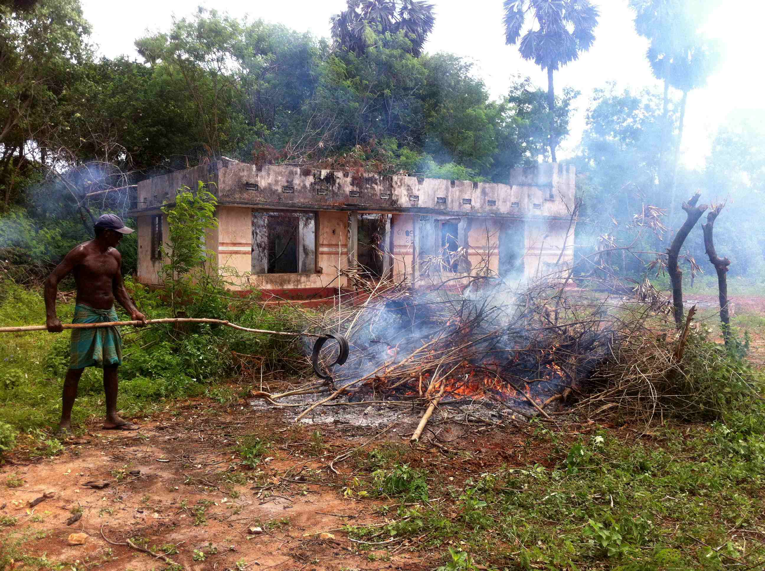 A man burns debris in front of a destroyed house on land returned to civilians by the military in Tellipallai, northern Sri Lanka