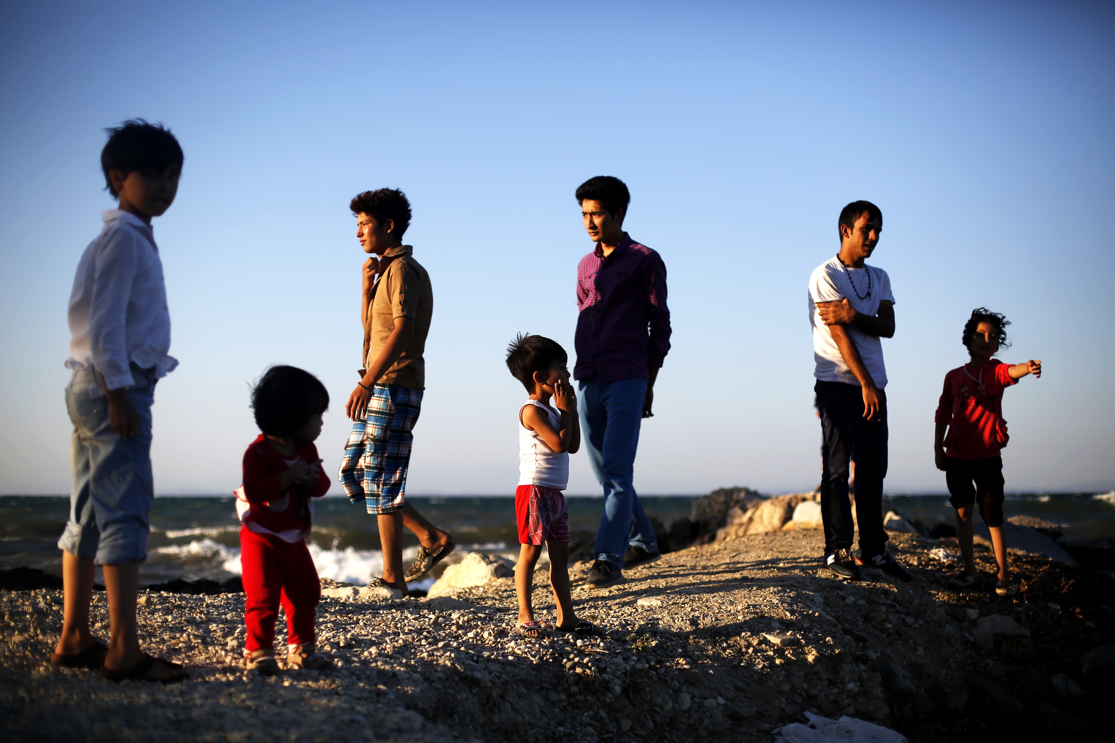 An extended family of Afghan asylum-seekers, newly arrived on Greece’s Lesvos Island, wait on the beach for police to register them. From here, they will continue onto Athens.