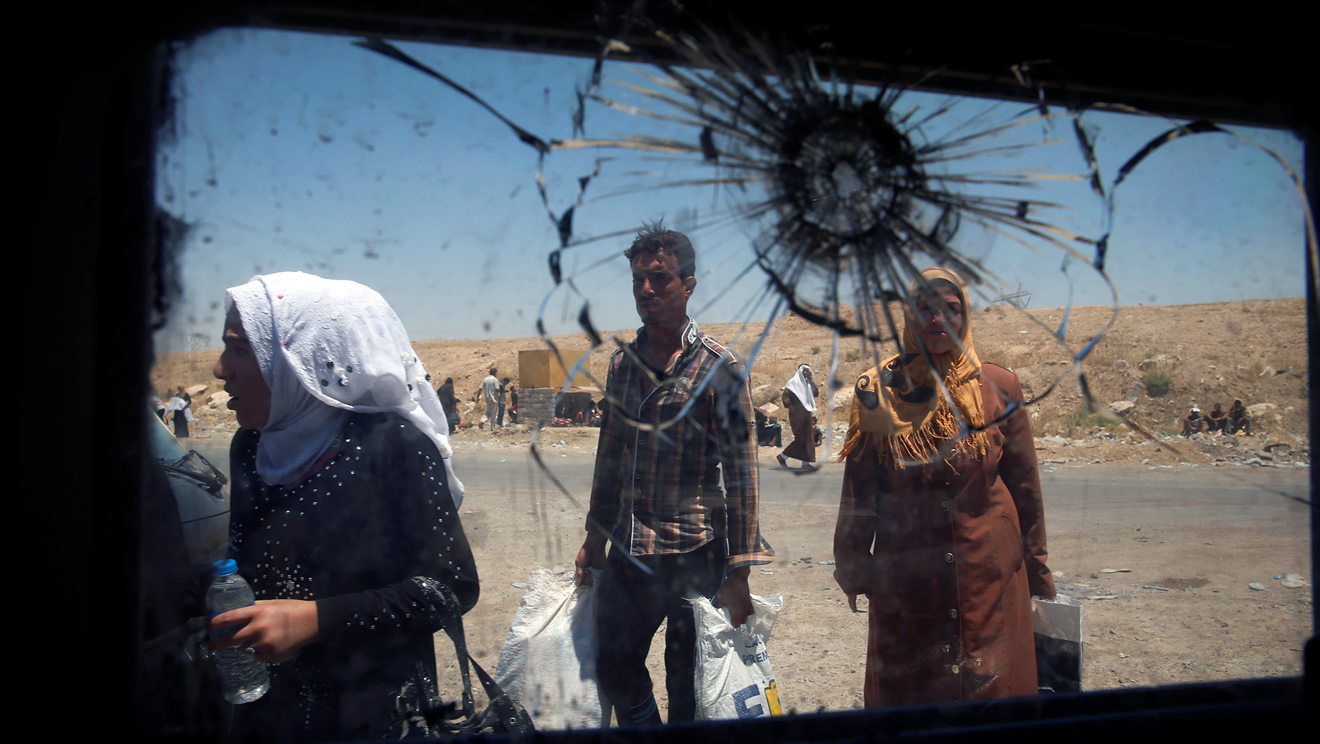 A few of several people through the back window of a car that is shattered with a bullet