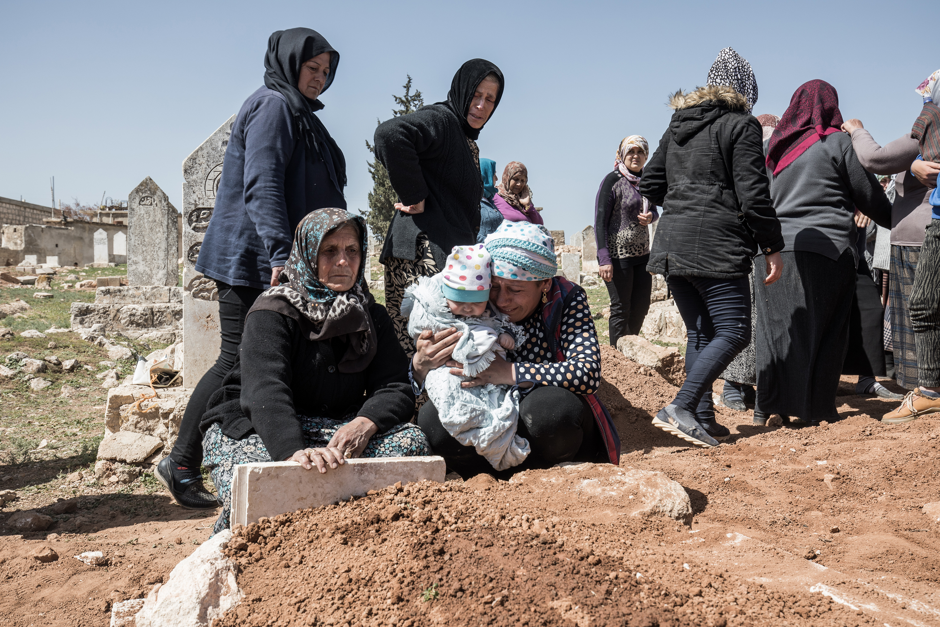 A woman grieves at a grave with others around her at other graves