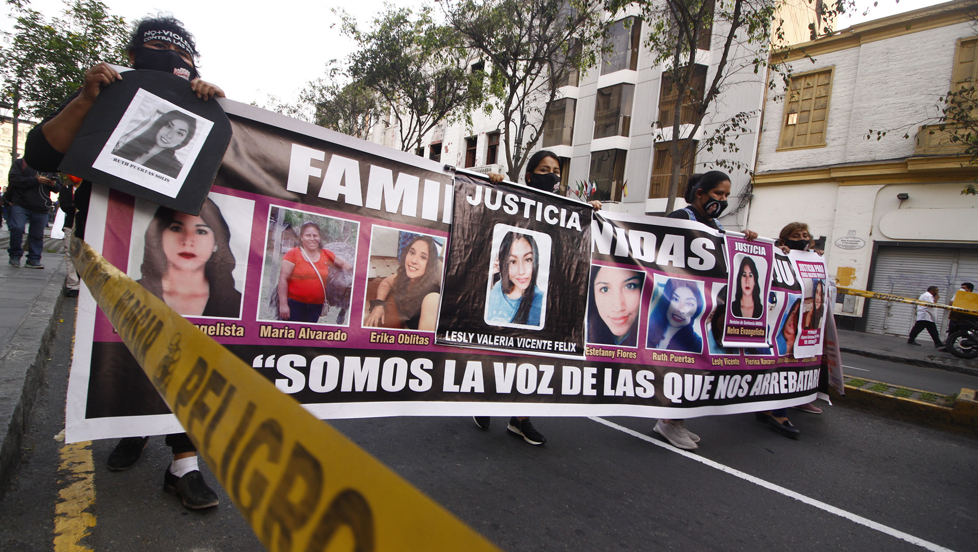 Image shows severl people holding a banner with faces of women and girls as they walk down a street.