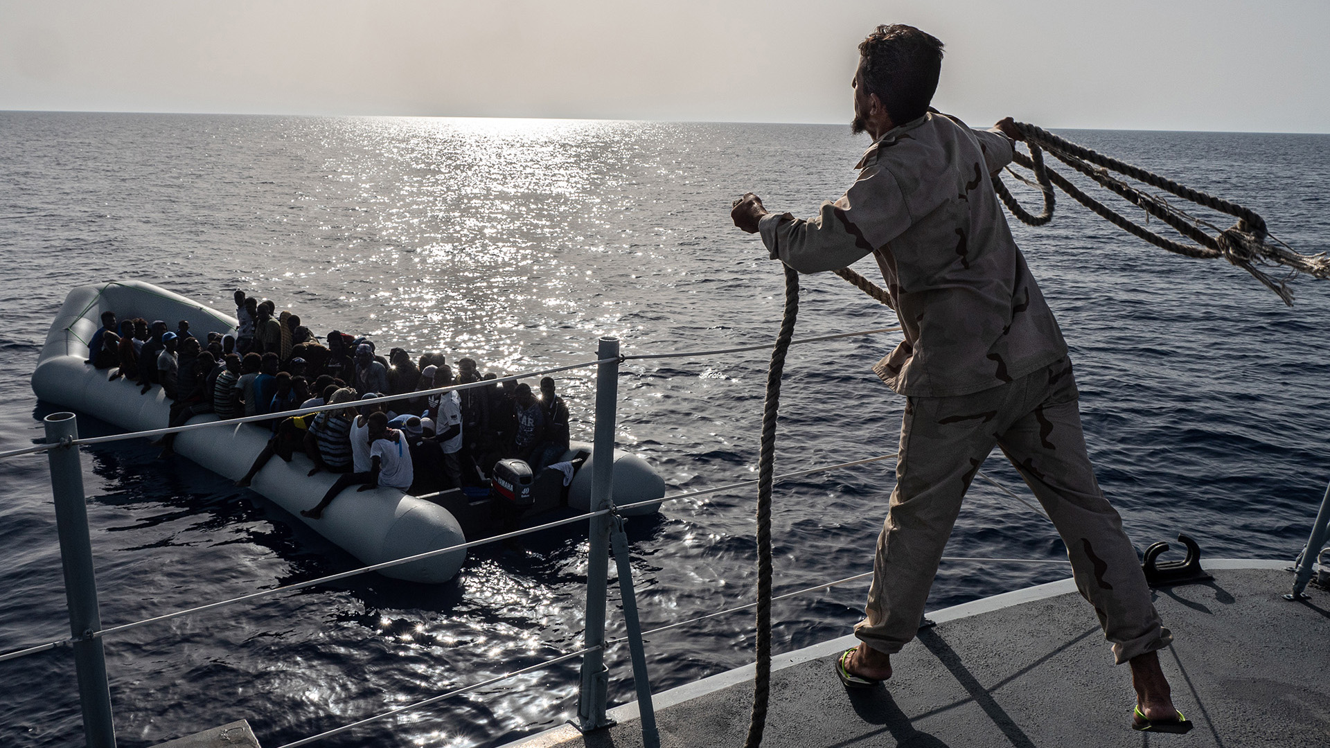 A Libyan Coast Guard sailor throws a rope towards boat carrying migrants