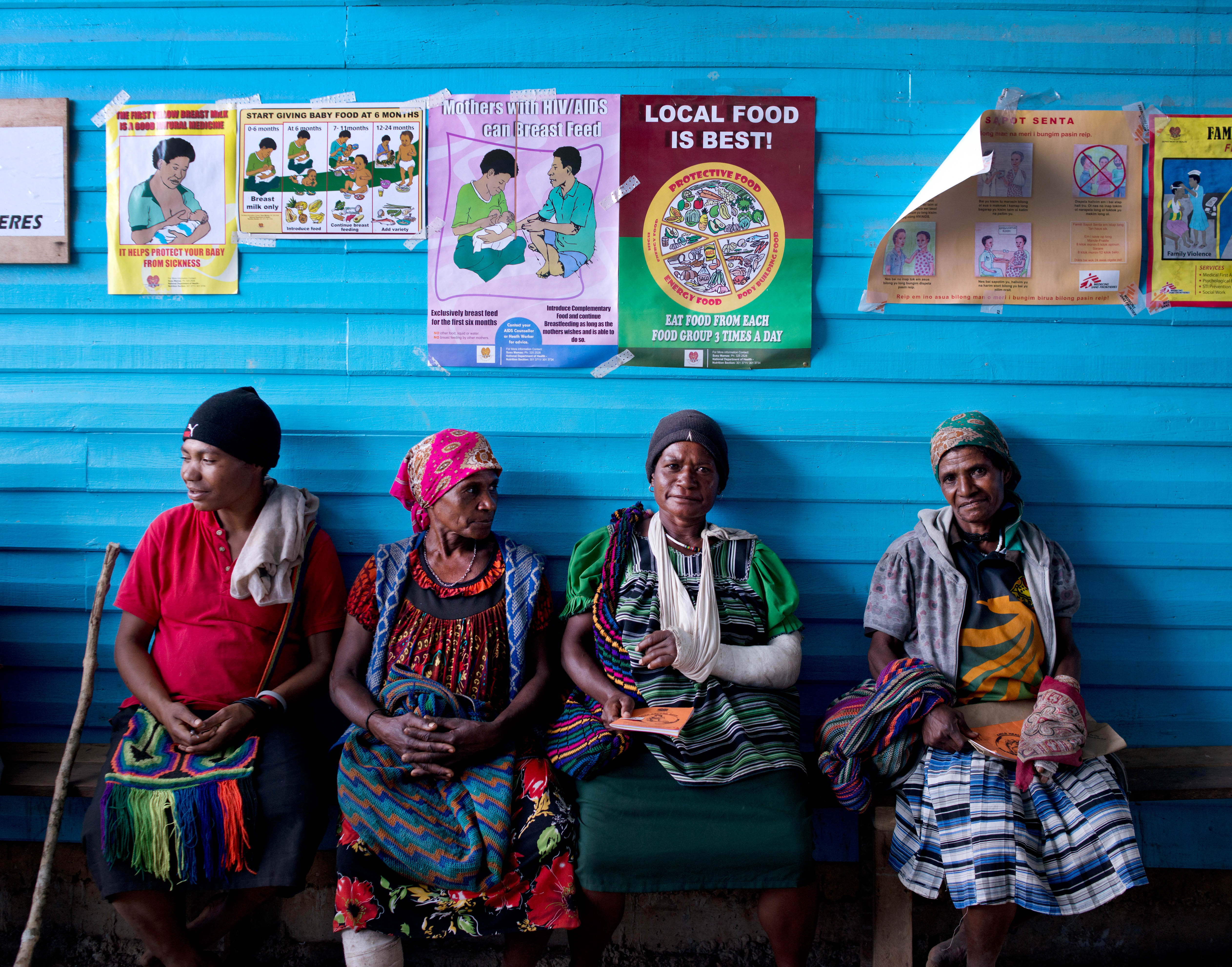 Four women await treatment on a bench in front of a blue wall outside the Surgical Ward at Tari Hospital in Papua New Guinea’s Hela Province
