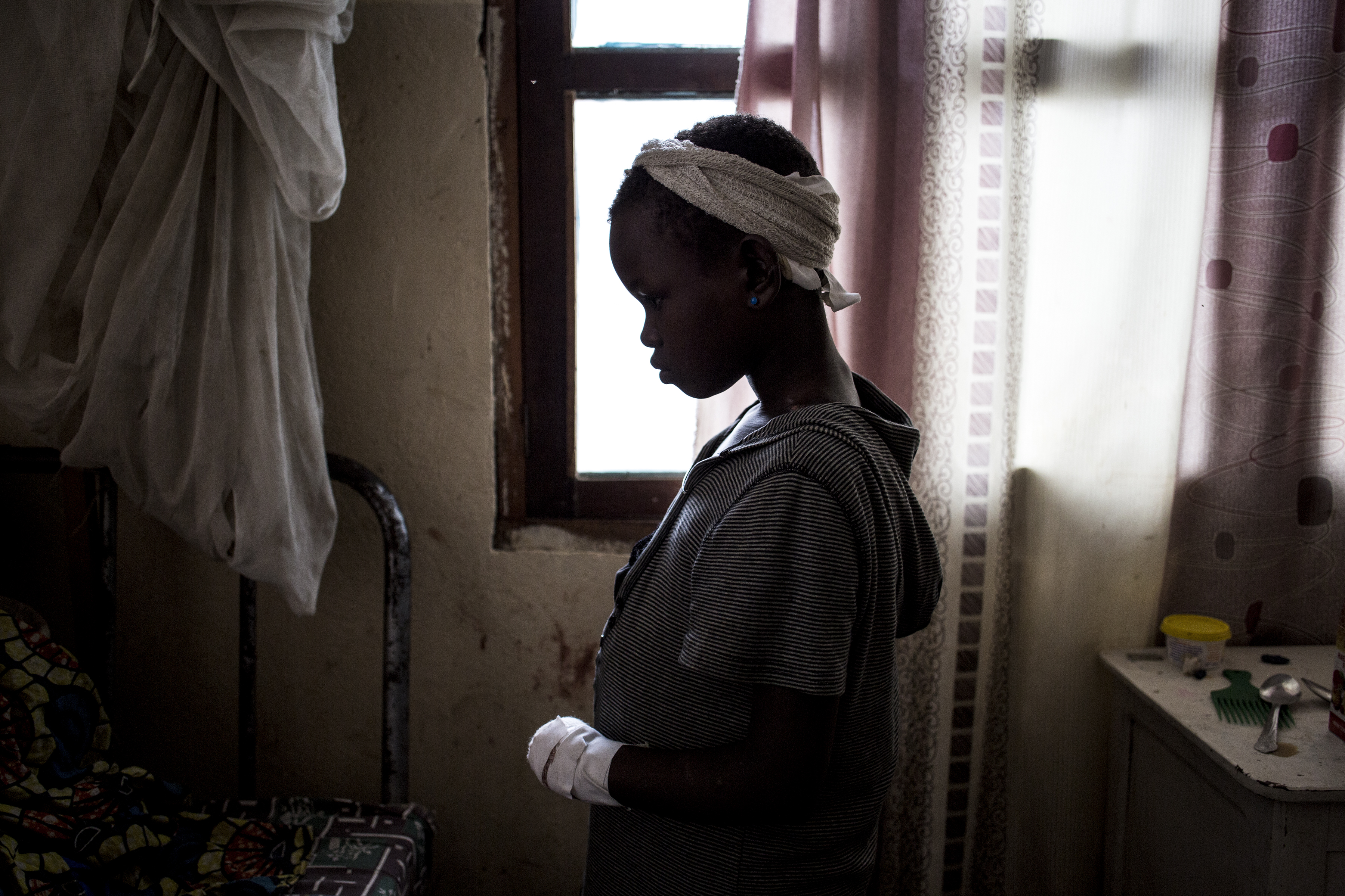 A silhouette profile of a young girl in a hospital looking down with bandages on her head and arm
