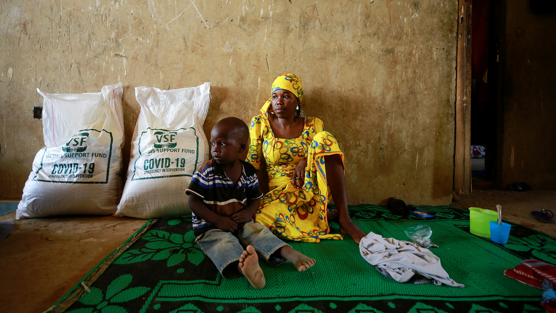 A woman and a child sit on the floor near some large sacks of aid.