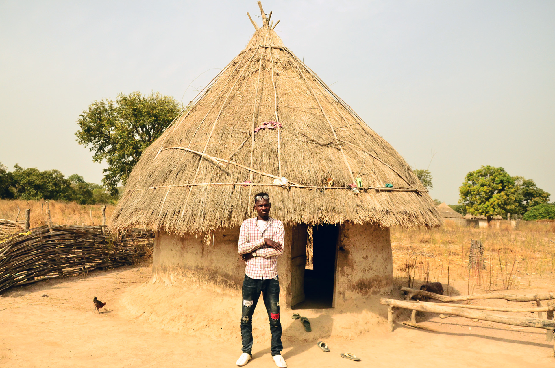 Ousmane Diallo stands in front of a thatched roof home in his village of Pakour, Senegal