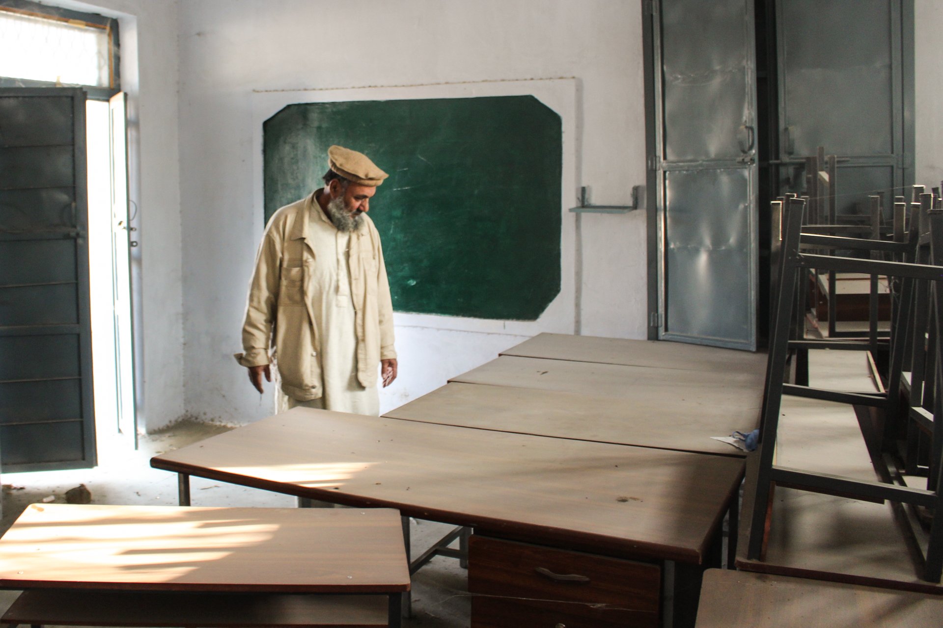 Hanif Ullah, a local education activist, inspects dust-covered desks and chairs at a shuttered school in Maminzo village, Pakistan.