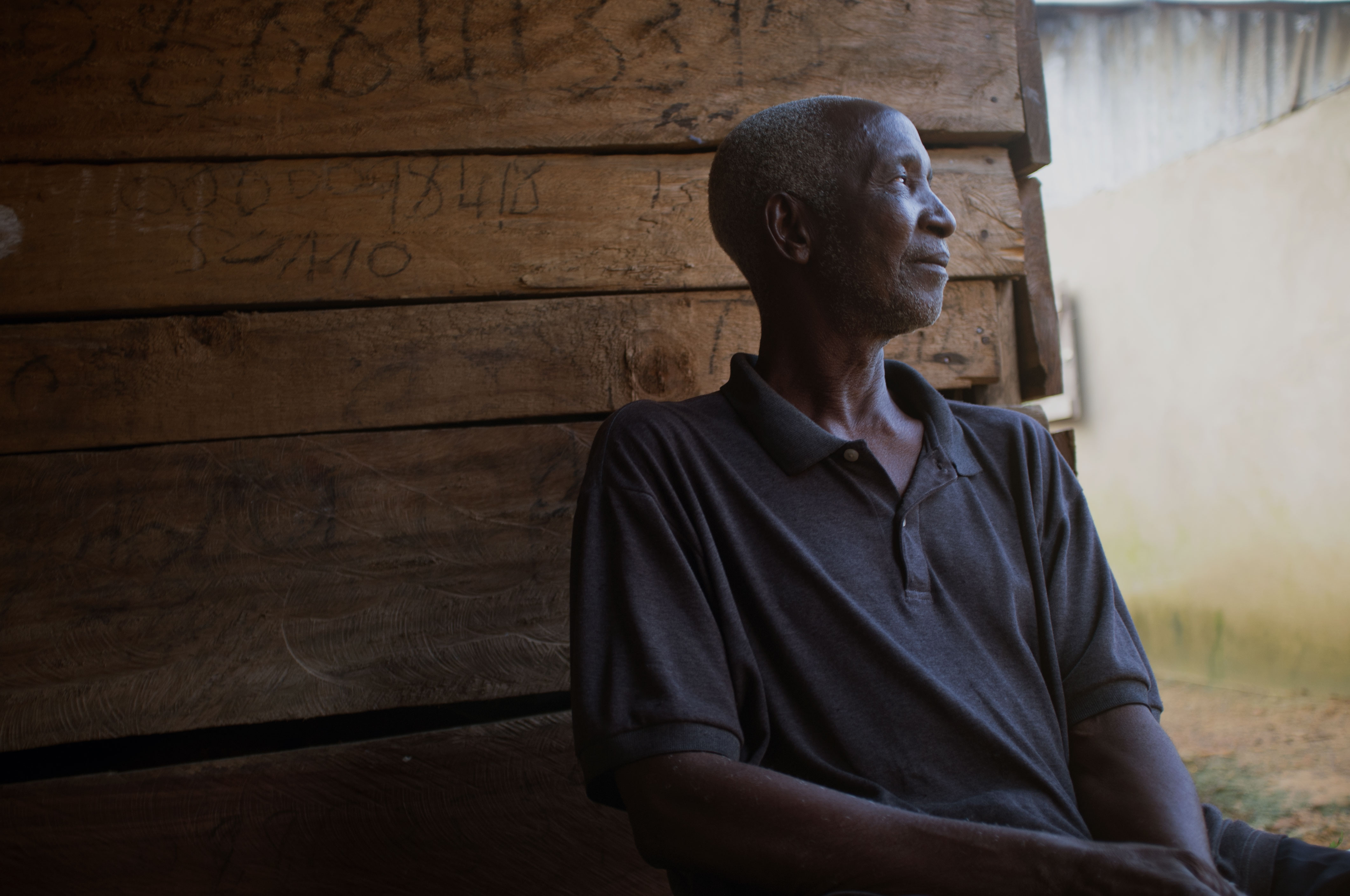 Yarpawolo Gblan sitting in front of his leaky temporary house where he has been living with his family for three years