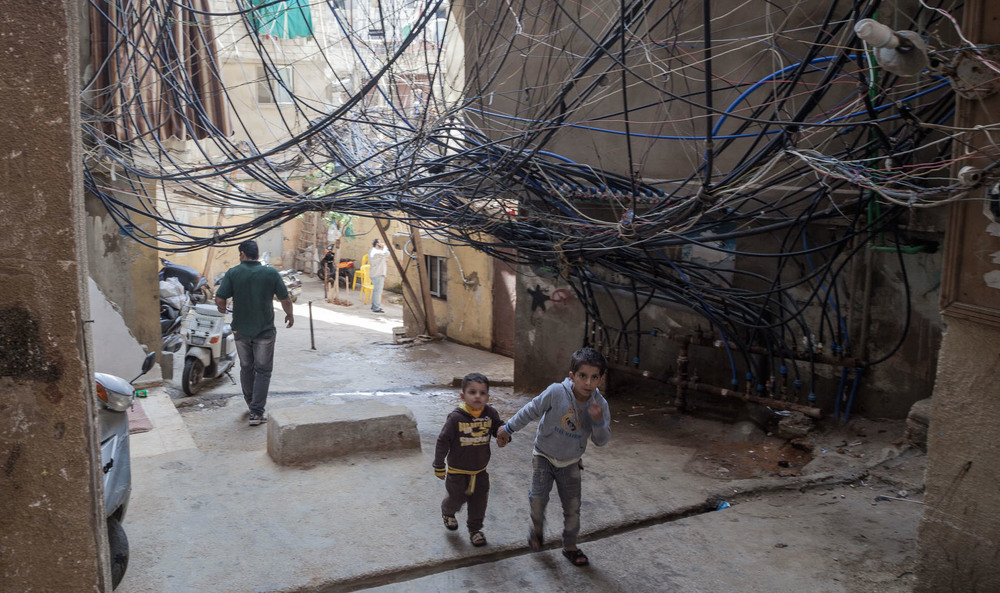 Two children walk under a nest of loose wires in the Bourj el-Barajneh neighborhood of Beirut.