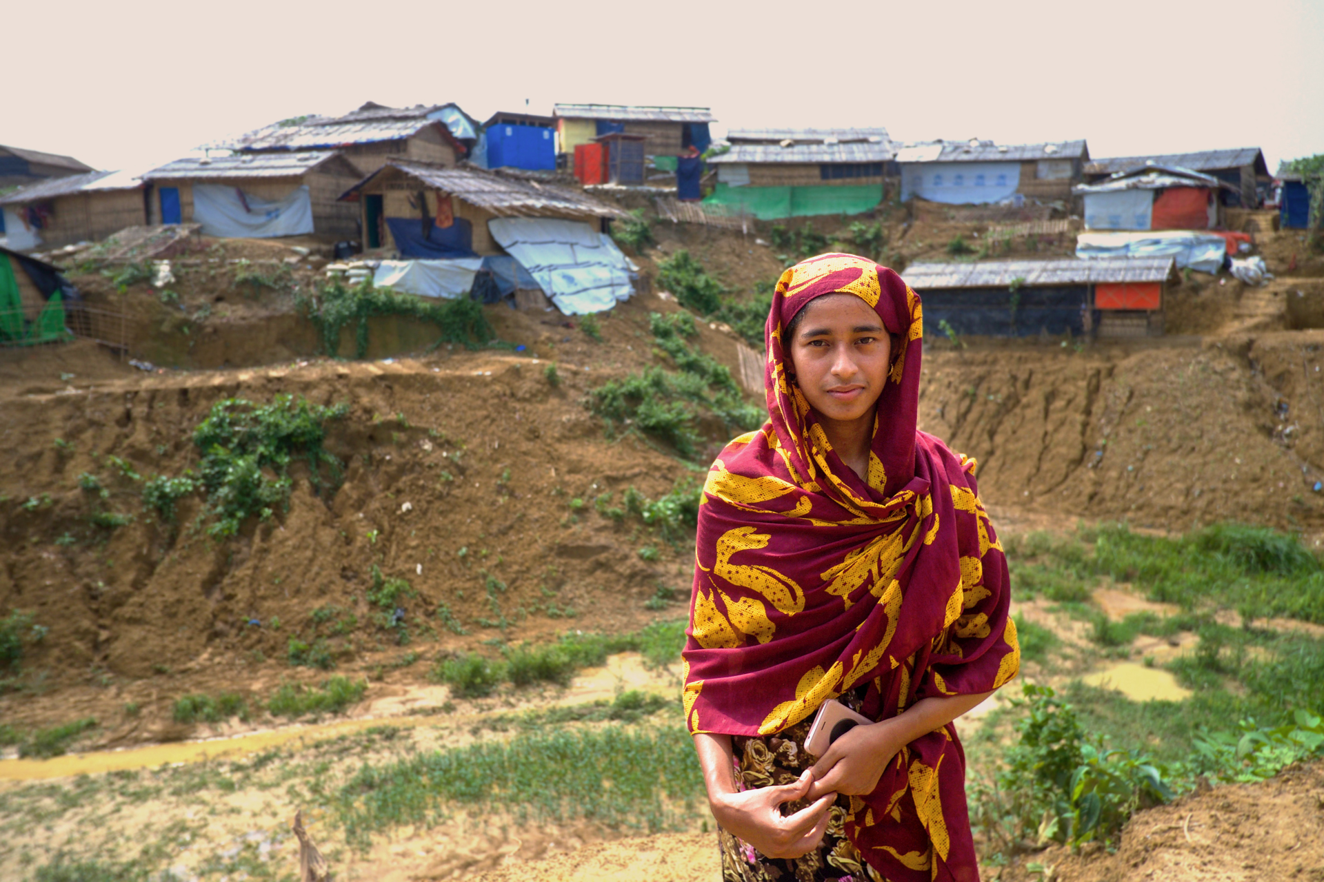 A woman looks at the camera in front of a refugee camp in Bangladesh