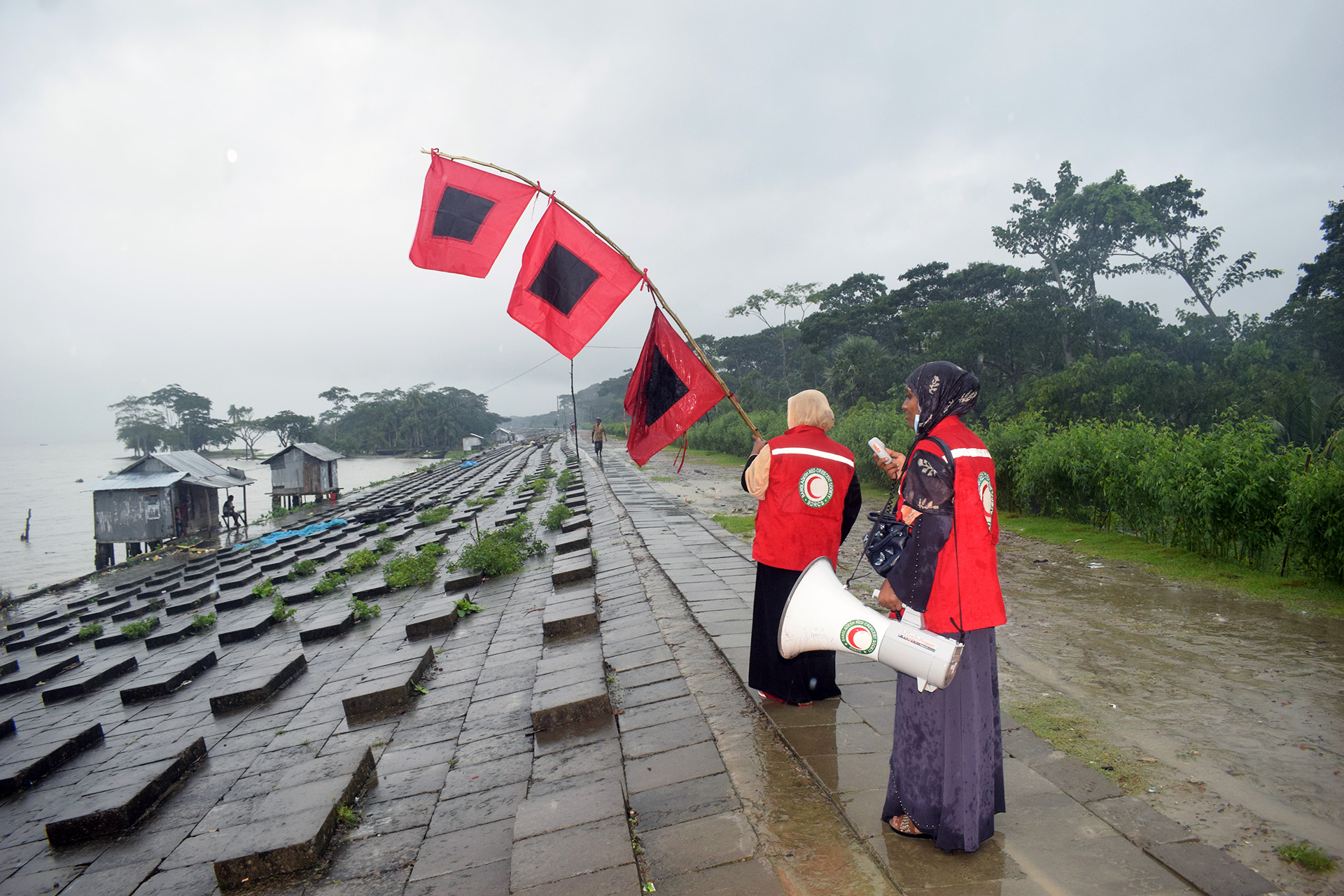 Two women holding tall red flags and a megaphone walk along a coastline.