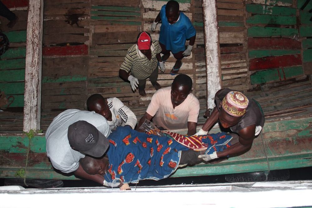 A sick person is being carried off of a boat wrapped in blanket.