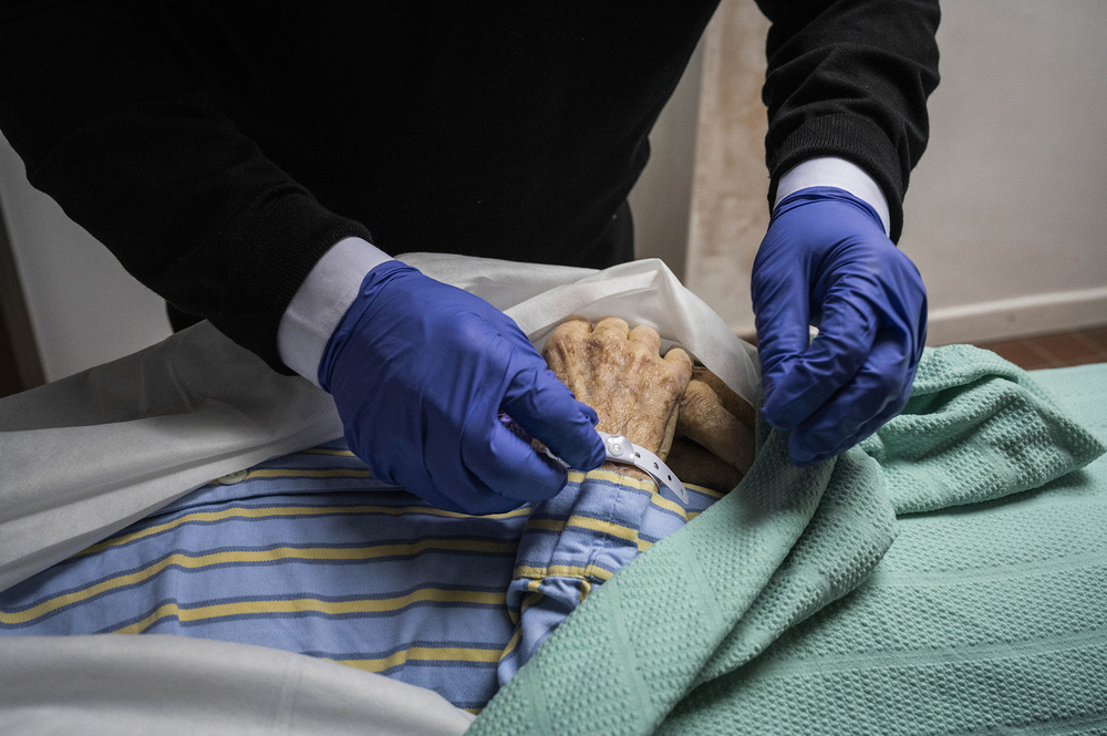 An employee of a funeral home attaches a name tag to the wrist of a patient who died that morning in a nursing home