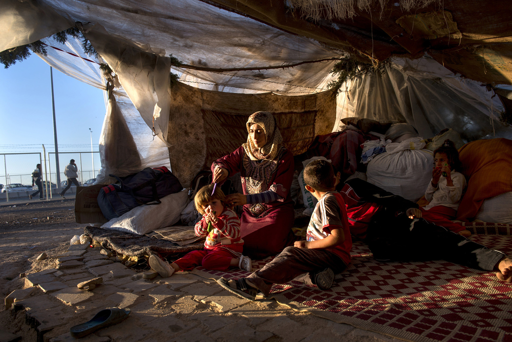 A mother and her children sit in their makeshift tent outside a displaced person’s camp on the Turkish border with Syria