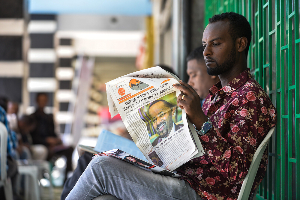 A man in Ethiopia sits reading a newspaper with Prime Minister Abiy's photo on the front.