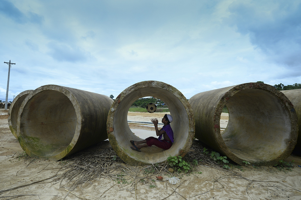 A Rohingya child plays with a football inside a sewage pipe at Kutupalong refugee camp in southern Bangladesh on 24 July 2019.