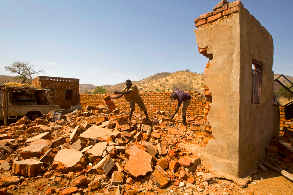 Civilians stand above a crater of a bomb