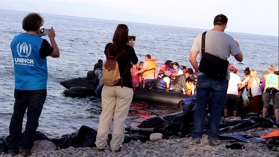 International aid workers take pictures as volunteers help arriving refugees from the boat