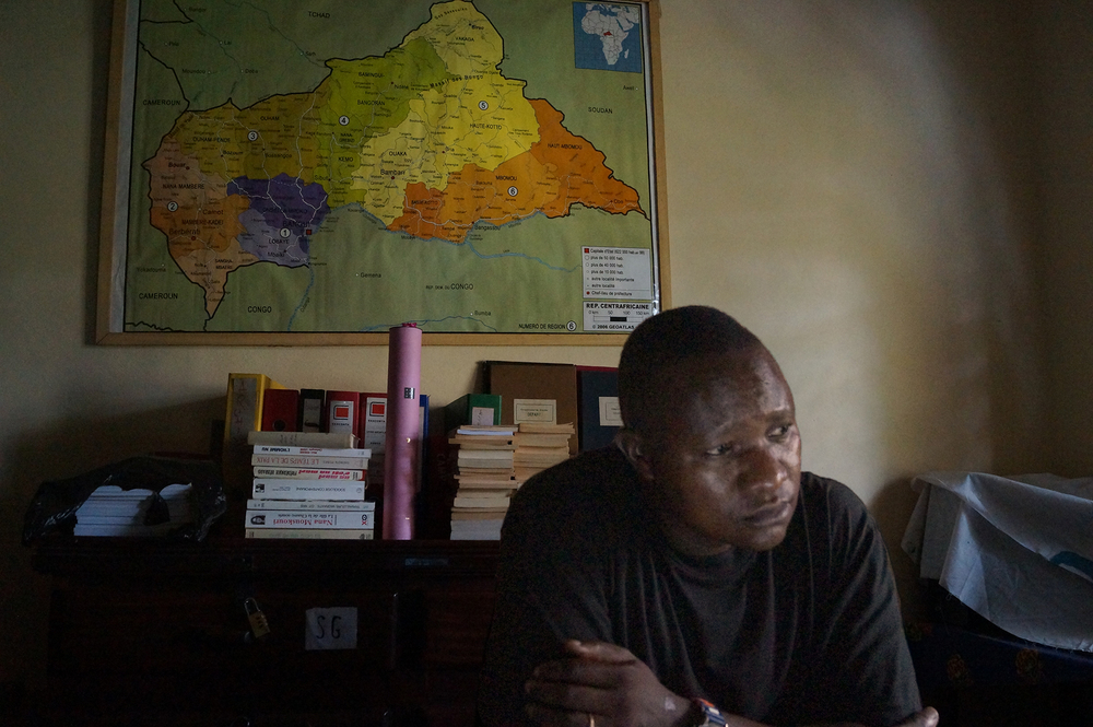 The young priest Frederic Nakombo sits in his office filled with case files, books and a large map of the Central African Republic on the wall behind him.