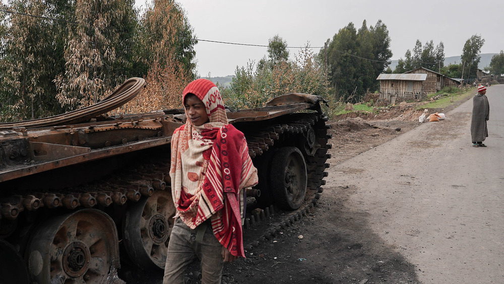 Residents walk past an abandoned tank on a main road in Amhara region, where hundreds of thousands of people have fled recent fighting.